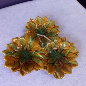 May include: A three-sectioned ceramic serving dish with a metal handle. The dish is decorated with a leafy design in shades of brown and green.