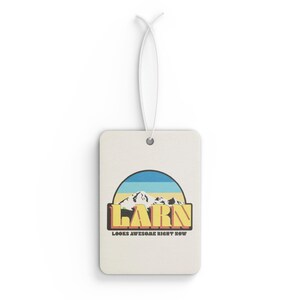 May include: A white car air freshener with a yellow, orange and blue mountain scene and the text "Larn Looks Awesome Right Now".