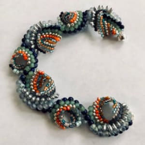 May include: A beaded bracelet featuring a spiral design with orange, teal, and silver beads. The bracelet is made of small, round beads and has a silver clasp. The bracelet's design is intricate and detailed.
