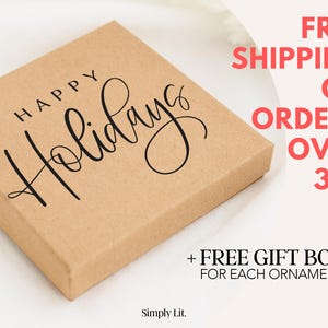 May include: A square, light brown box with the words "HAPPY Holidays" in black script. The box is on a white surface. The text "Simply Lit" is at the bottom left.
