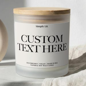 May include: A frosted glass candle with a wooden lid. The label reads "Simply Lit." with the words "CUSTOM TEXT HERE" in large, bold letters. The bottom of the label states "ECO FRIENDLY | VEGAN | MADE IN USA NATURAL SOY WAX CANDLE."