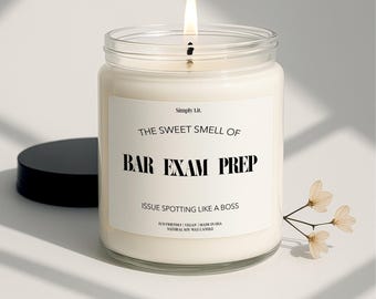 May include: A lit candle in a clear glass jar with a black lid. The label reads "THE SWEET SMELL OF BAR EXAM PREP" and "ISSUE SPOTTING LIKE A BOSS". A small sprig of flowers is next to the candle. The candle is made in the USA.