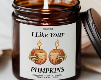 May include: A lit soy wax candle in a brown glass jar with a black lid. The label reads "I Like Your Pumpkins" with a graphic of two pumpkins held by skeleton hands. The candle is eco-friendly, vegan, and made in the USA.