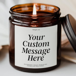 May include: A lit brown glass jar candle with a black lid. The candle has a white label with the text "Your Custom Message Here" and "Simply Lit." The candle is made of natural soy wax.