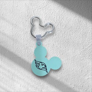 May include: A light blue Mickey Mouse-shaped keychain with a silver-colored key ring. The keychain features a black wing design with a Mickey Mouse silhouette. The background is a textured white surface.