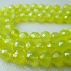 May include: A strand of faceted, round beads in a vibrant, translucent yellow-green color. The beads have a polished, glossy finish, and are strung together on a thin, light-yellow cord. The beads are approximately 8mm in diameter.