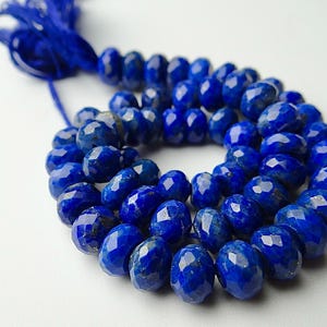 Pu&ograve; includere: Un filo di perline di lapislazzuli blu intenso sfaccettate. Le perline di forma ovale sono infilate con un cordino blu abbinato. Lo sfondo &egrave; una superficie bianca e liscia. Le perline hanno un diametro di circa 8 mm.