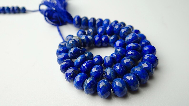 Pu&ograve; includere: Un filo di perline di lapislazzuli blu intenso sfaccettate. Le perline di forma ovale sono infilate con un cordino blu abbinato. Lo sfondo &egrave; una superficie bianca e liscia. Le perline hanno un diametro di circa 8 mm.