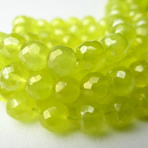 May include: Close-up of a strand of faceted, chartreuse-colored beads. The beads are round and have a sparkling, gem-like appearance. The beads are strung on a matching chartreuse cord, suggesting jewelry making supplies.
