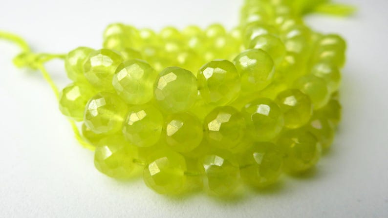 May include: Close-up of a strand of faceted, chartreuse-colored beads. The beads are round and have a sparkling, gem-like appearance. The beads are strung on a matching chartreuse cord, suggesting jewelry making supplies.