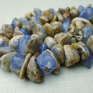 May include: A close-up of a bracelet made of polished, irregular-shaped stones. The stones are a mix of light blue and tan colors. The bracelet is lying on a light-colored surface.