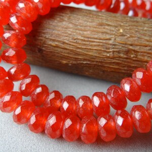 May include: Close-up of a strand of faceted, vibrant red beads. The beads are strung together, creating a necklace or bracelet. The beads have a sparkling, gem-like quality, reflecting light. The background includes a wooden element.