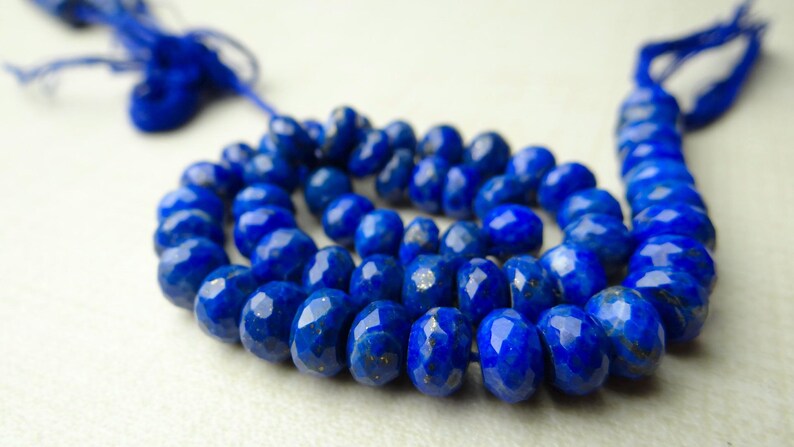 Pu&ograve; includere: Una collana di perline sfaccettate di lapislazzuli blu intenso. Le perline di forma ovale sono infilate con un cordoncino blu, adatte per una collana o un braccialetto. Le perline hanno una superficie lucida e riflettente.