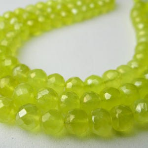 May include: A strand of faceted, chartreuse-colored beads. The beads are round with multiple facets, giving them a sparkling appearance. The beads are strung together, with a tassel at the end. The background is a soft, neutral color.