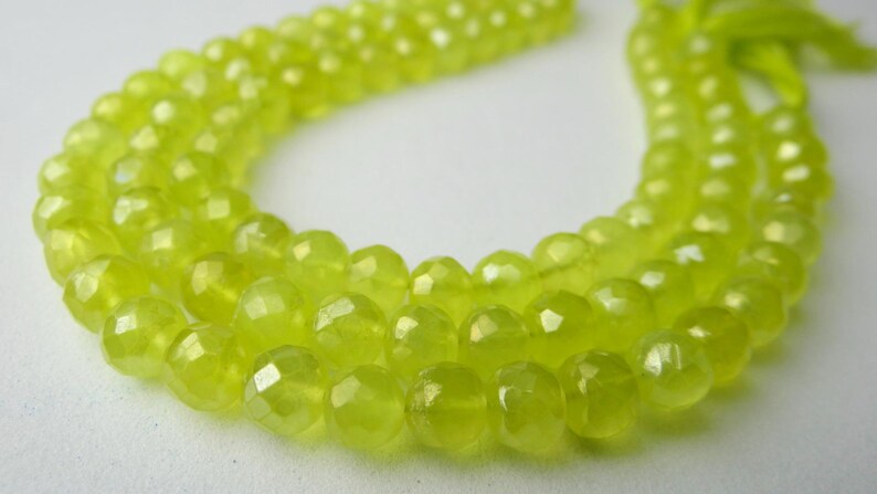 May include: A strand of faceted, chartreuse-colored beads. The beads are round with multiple facets, giving them a sparkling appearance. The beads are strung together, with a tassel at the end. The background is a soft, neutral color.
