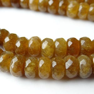 Peut inclure: Un collier de perles en pierre gemme facettées, rondes et de couleur ambre, disposées en ligne courbe. Chaque perle présente une surface polie et translucide avec de subtiles variations internes et un trou central pour l'enfilage.
