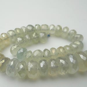 K&ouml;nnte beinhalten: Eine Kette aus facettierten, hellgr&uuml;nen Edelsteinperlen. Die Perlen sind aufgef&auml;delt und bilden eine spiralf&ouml;rmige Form. Am Ende der Kette ist eine blaue Quaste befestigt. Die Perlen haben eine durchscheinende Qualit&auml;t und einen subtilen Glanz.