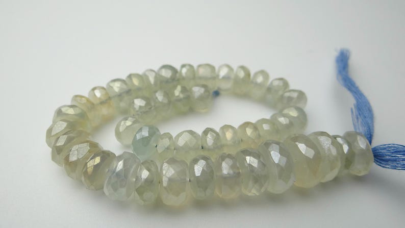 K&ouml;nnte beinhalten: Eine Kette aus facettierten, hellgr&uuml;nen Edelsteinperlen. Die Perlen sind aufgef&auml;delt und bilden eine spiralf&ouml;rmige Form. Am Ende der Kette ist eine blaue Quaste befestigt. Die Perlen haben eine durchscheinende Qualit&auml;t und einen subtilen Glanz.