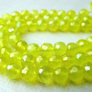 May include: A strand of faceted, chartreuse-colored beads. The beads are round with multiple facets, creating a sparkling effect. The beads are strung together, forming a necklace or bracelet.