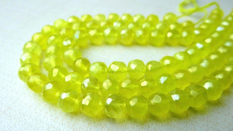 May include: A strand of faceted, chartreuse-colored beads. The beads are round with multiple facets, creating a sparkling effect. The beads are strung together, forming a necklace or bracelet.