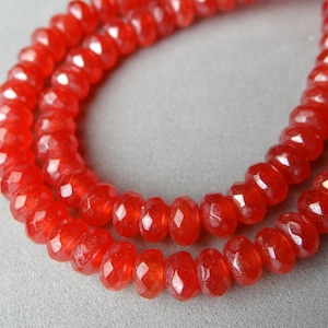May include: A strand of faceted, bright red beads. The beads are small, round, and strung together, creating a necklace-like appearance. The beads have a glossy finish and reflect light.