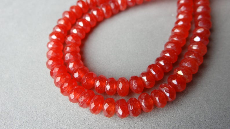 May include: A strand of faceted, bright red beads. The beads are small, round, and strung together, creating a necklace-like appearance. The beads have a glossy finish and reflect light.