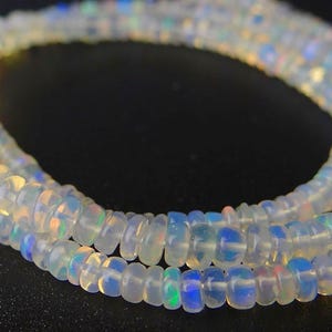 Puede incluir: Un collar de cuentas de piedras preciosas opalescentes. Las cuentas son pequeñas, redondas y translúcidas, con destellos de color iridiscente. Las cuentas están ensartadas, formando un collar o pulsera.