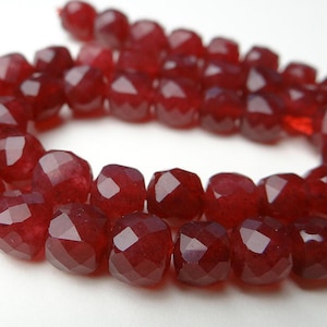 May include: A strand of faceted, deep red gemstone beads. The beads are a rich, dark red color and have a multi-faceted cut that catches the light. The beads are strung together, forming a necklace or bracelet.