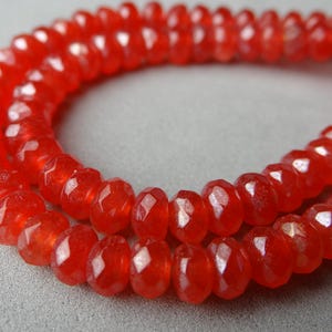 May include: Close-up of a strand of faceted, bright red beads. The beads are small, round, and have a polished, reflective surface. The beads are strung together, forming a necklace or bracelet.