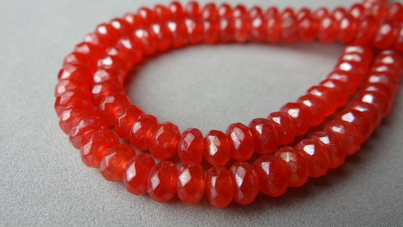 May include: Close-up of a strand of faceted, bright red beads. The beads are small, round, and have a polished, reflective surface. The beads are strung together, forming a necklace or bracelet.