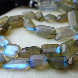 May include: A strand of faceted labradorite beads. The beads are a mix of translucent gray-brown with flashes of blue and iridescent color. The beads are strung together with a black tassel at the top.