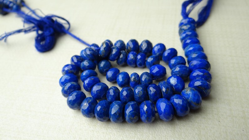 Pu&ograve; includere: Una collana di perline sfaccettate di lapislazzuli blu intenso. Le perline sono disposte a spirale, con un nappa di filo blu a ciascuna estremit&agrave;. Le perline hanno una superficie lucida e riflettente.