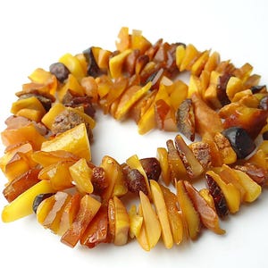May include: A bracelet composed of numerous irregular, polished amber chips in varying shades of yellow, orange, and deep brown. The translucent and opaque pieces are strung together to form a circular shape with a textured, multi-faceted surface.