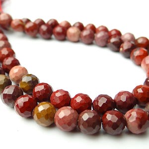 May include: A strand of faceted gemstone beads in shades of red, brown, and pink. The beads are strung together, with a red tassel at the end. The beads are approximately 8mm in diameter.