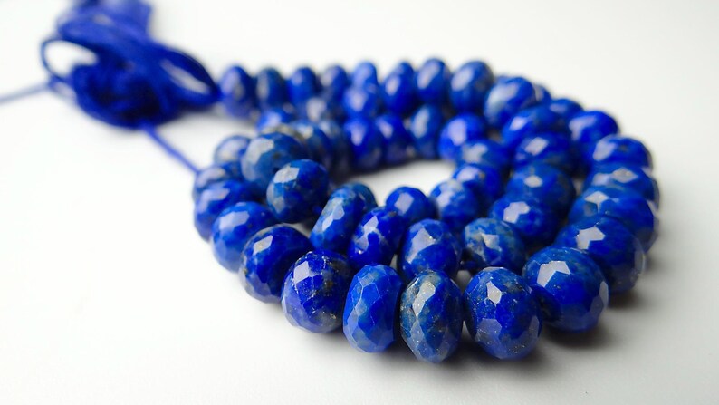 Pu&ograve; includere: Una collana di perline di lapislazzuli blu intenso sfaccettate. Le perline sono di un blu ricco e saturo con una superficie lucida e riflettente. Le perline sono infilate con un cordoncino blu abbinato, creando una collana di pietre preziose.