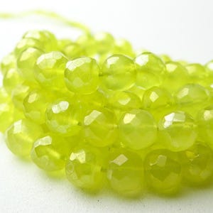 May include: Close-up of a strand of faceted, chartreuse-colored gemstone beads. The beads are round with multiple facets, creating a sparkling effect. The beads are strung together, ready for jewelry making.