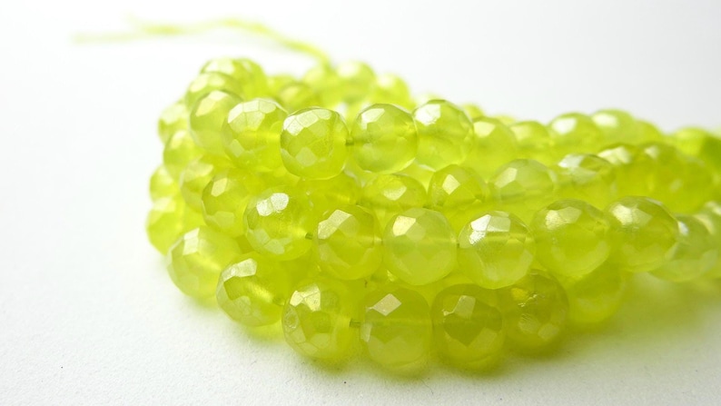 May include: Close-up of a strand of faceted, chartreuse-colored gemstone beads. The beads are round with multiple facets, creating a sparkling effect. The beads are strung together, ready for jewelry making.