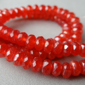 May include: Close-up of a strand of faceted, red gemstone beads. The beads are strung together, forming a necklace or bracelet. The beads have a glossy, transparent appearance, and the color is a vibrant, warm red.