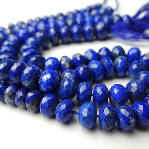 Pu&ograve; includere: Un filo di perline sfaccettate di lapislazzuli blu intenso. Le perline di forma ovale sono infilate insieme, con un nappa blu abbinata all'estremit&agrave;. Le perline hanno una superficie lucida e riflettente.