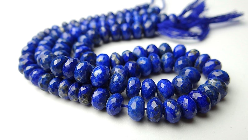 Pu&ograve; includere: Un filo di perline sfaccettate di lapislazzuli blu intenso. Le perline di forma ovale sono infilate insieme, con un nappa blu abbinata all'estremit&agrave;. Le perline hanno una superficie lucida e riflettente.