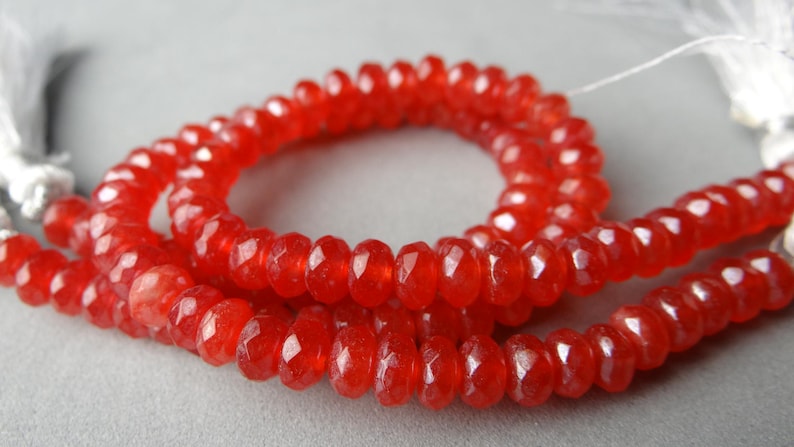May include: Strands of faceted, vibrant red gemstone beads. The beads are strung together, forming a necklace or bracelet. The beads have a sparkling, polished appearance, and are displayed against a neutral background.