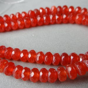 May include: A strand of faceted, vibrant red beads. The beads have a symmetrical, rounded shape and a polished, reflective surface. The beads are strung together, forming a necklace or bracelet.