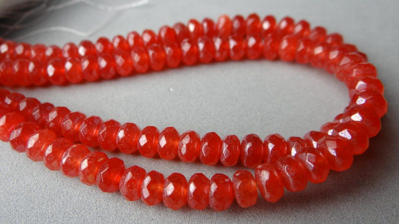 May include: A strand of faceted, vibrant red beads. The beads have a symmetrical, rounded shape and a polished, reflective surface. The beads are strung together, forming a necklace or bracelet.