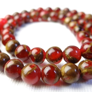 May include: A strand of round beads in shades of red and brown. The beads have a glossy finish and appear to be made of a translucent material. The beads are arranged in a circular pattern, suggesting a necklace or bracelet.