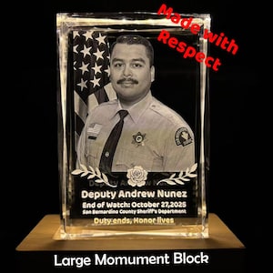 May include: A large, clear monument block with a photo of Deputy Andrew Nunez, an American flag, and text that reads "Duty ends, Honor lives." The words "Made with Respect" are in red. The base is a light brown color.