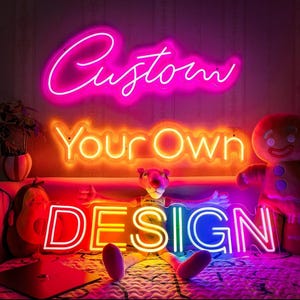 May include: Neon signs spelling "Custom", "Your Own", and "Design" in bright pink, orange, and blue. The signs are arranged above a bed with stuffed animals. The word "Custom" is in a cursive font.