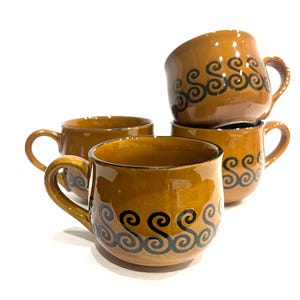 May include: A set of four brown ceramic mugs with black swirl designs. Each mug has a rounded body, a handle, and a glossy finish. The mugs are stacked and arranged on a white background.