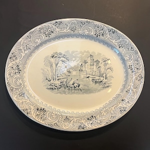 May include: Oval serving platter with a black and white landscape scene. The center features a river with people in a boat, trees, and a castle. The border has a floral and scroll design.