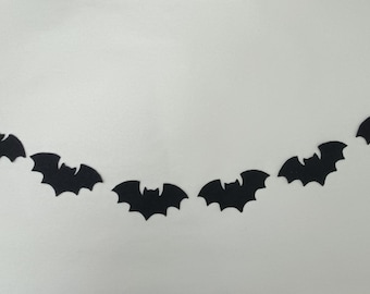 May include: A decorative garland of black bat silhouettes, arranged in a curved pattern against a white backdrop. The bats are uniformly spaced and feature a simple design. Ideal for Halloween, this garland adds a spooky atmosphere.