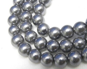 May include: A strand of round, metallic dark gray beads arranged in a curved formation. Each bead features a smooth, reflective surface with a high-gloss finish, creating a uniform appearance across the entire length of the beaded string.